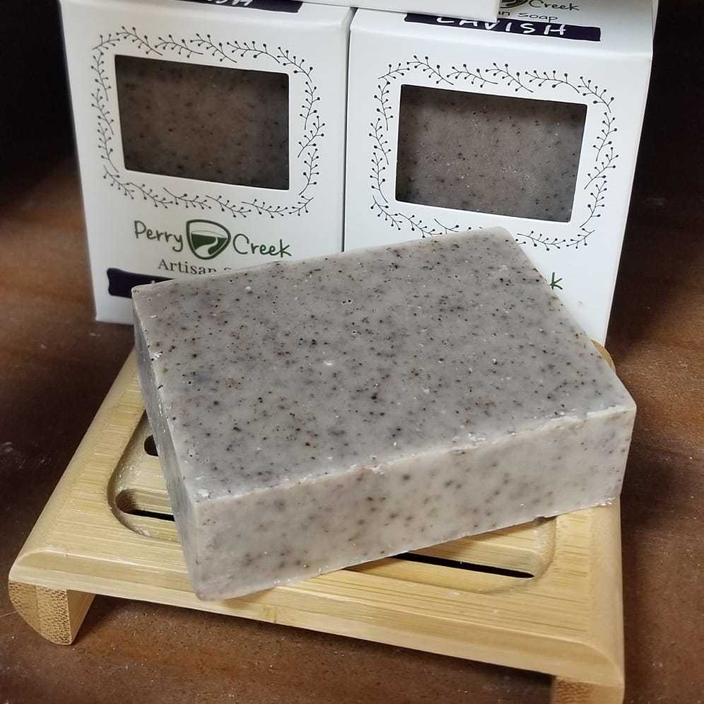 A bar of peppermint and lavender scented soap sitting on an ecofriendly bamboo soap dish with other essential oil scented bars stacked behind